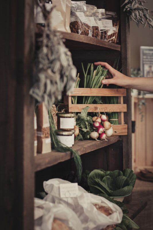 Hand sträcker sin efter färska grönsaker i en hylla fylld med lokal mat