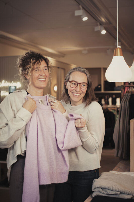 Två glada kvinnor håller i en tröja i en klädbutik